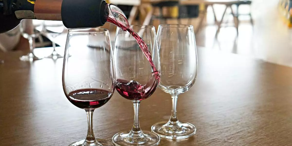A bottle of Cotes du Rhone or Pinot Noir is being poured into a glass of wine.