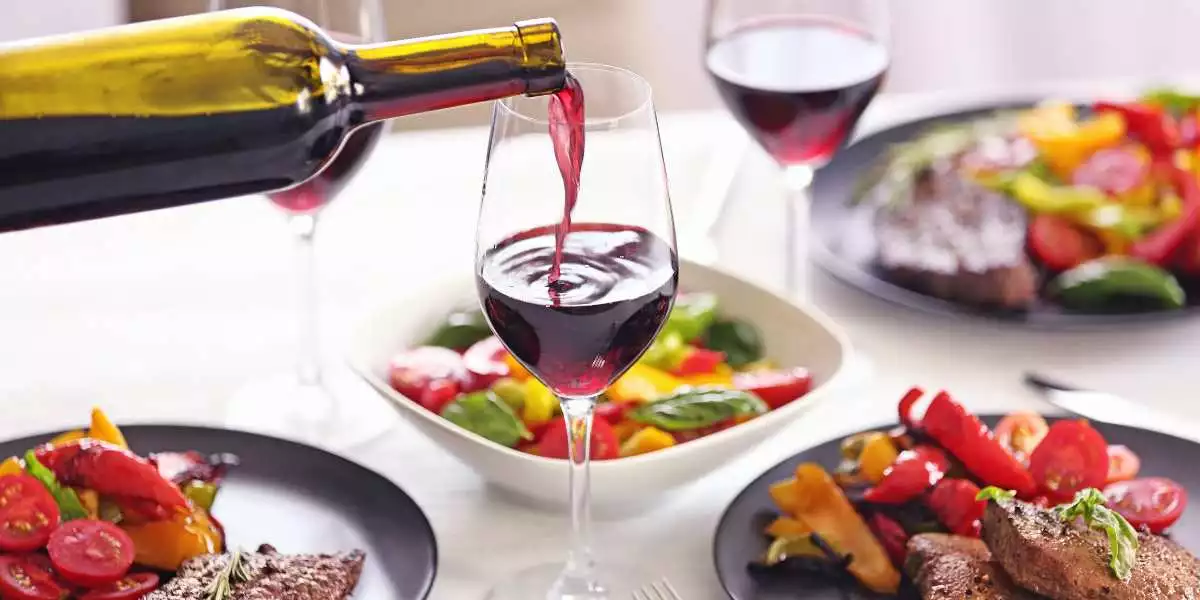 A glass of red wine is being poured onto a plate of food.