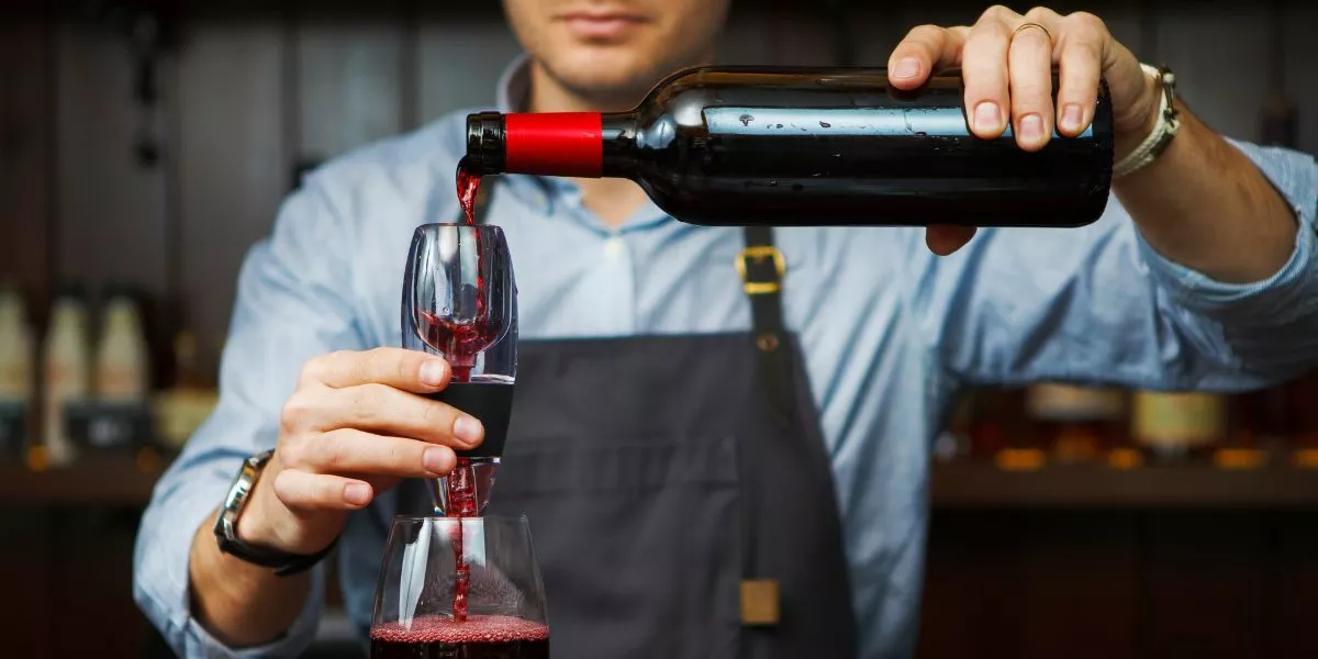 A bartender pouring red wine into a glass with wine-aerator