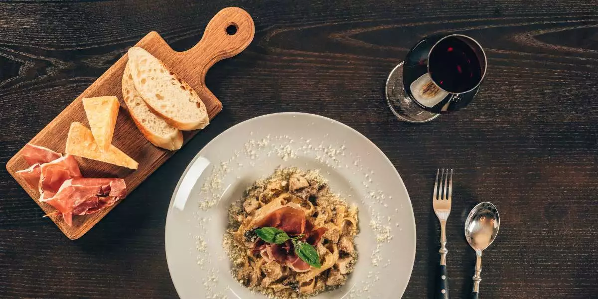 A plate of pasta with meat and wine on a wooden table.