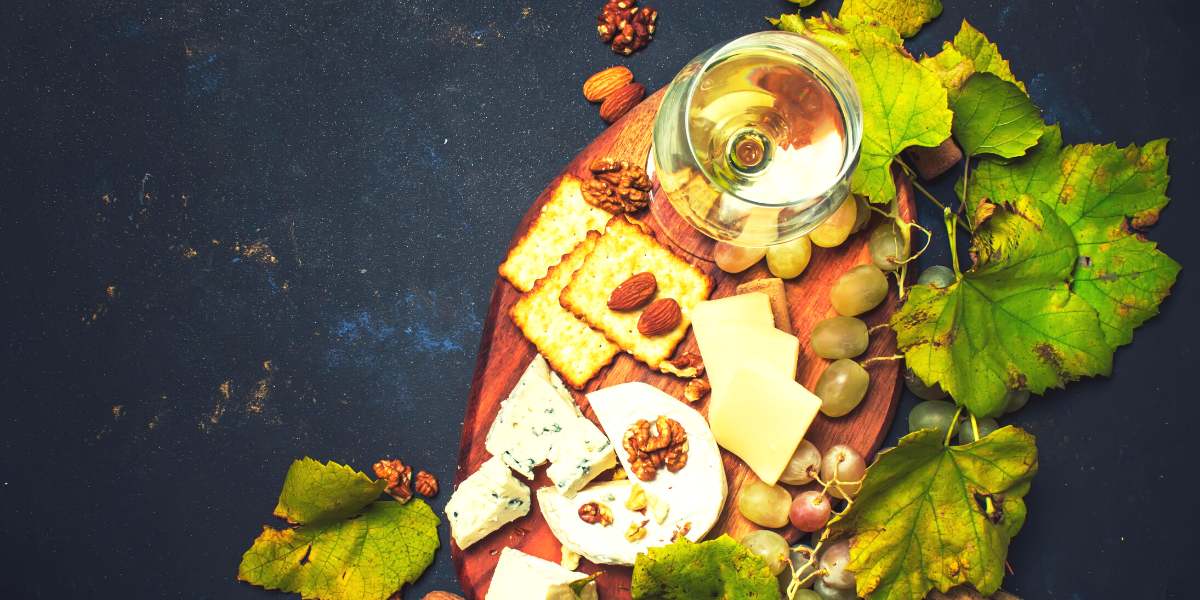 Wine, cheese, nuts and grapes on a wooden board.