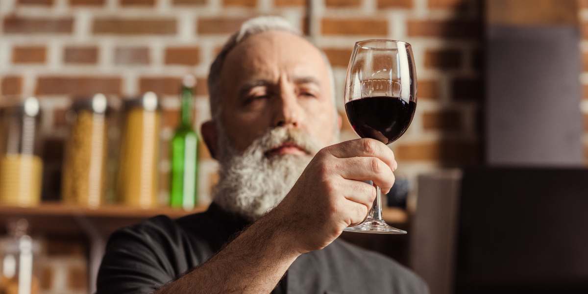 A man with a beard is holding a glass of wine.